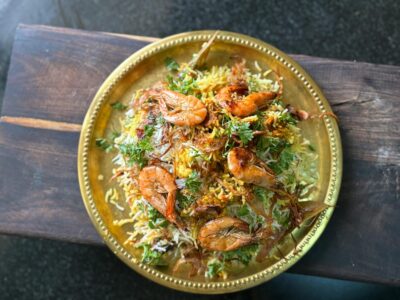A vibrant plate of shrimp biryani with herbs, beautifully presented on a golden platter, shot from above.